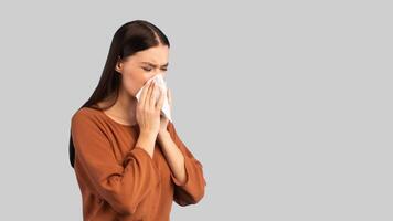 Cold And Flu. Sick Woman Blowing Runny Nose In Paper Tissue Having Rhinitis Symptom Standing On Blue Studio Background. Lady Sneezing Suffering From Allergy. Panorama, Empty Space photo