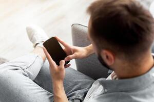 Above view of young guy using smartphone with blank screen at home, mockup for mobile app design. Millennial man holding modern gadget, empty space for website or advertisement photo
