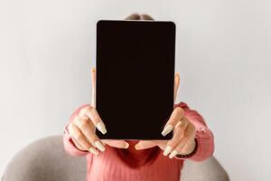 Millennial woman showing digital tablet with blank screen on white studio background, mockup for website or app design. Young lady presenting touch pad with space for online advertisement, closeup photo