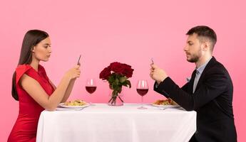 Boring Date. Couple Using Cellphones During Dinner Sitting At Table Posing Over Yellow Background In Studio. photo