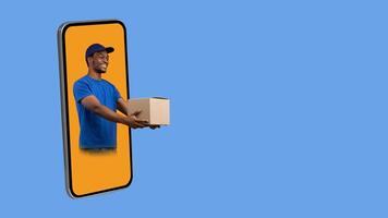Parcel Shipping App. Black Deliveryman In Phone Screen Giving Cardboard Box To The Side Delivering Package Over Yellow Studio Background. Collage, Panorama With Free Space For Text photo