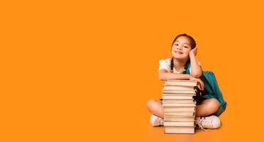 Back To School. Cute Asian Elementary Student Girl Sitting At Books Stack Over Yellow Studio Background. Panorama, Copy Space photo