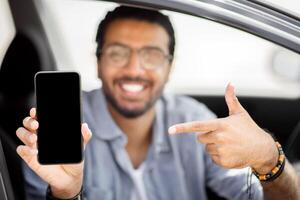 Happy indian man driver holding smartphone with blank screen, mockup. Closeup of mobile phone with empty display in smiling middle-eastern guy hand, using mobile app for navigation, copy space photo