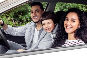 Smiling young arab man and woman with child are driving in car and looking at camera from open window, outdoor, panorama. Travel with family in summer, road and vacation together travel by automobile photo
