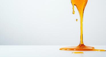 Warm golden honey flows and splashes onto a clean white surface, creating beautiful liquid shapes. The sunlit background enhances the vibrant color, highlighting its smooth texture. photo