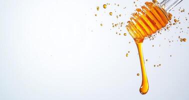 Golden honey drips from a wooden dipper, creating splashes of liquid in the air. The smooth texture and vibrant color contrast beautifully with the light backdrop. photo