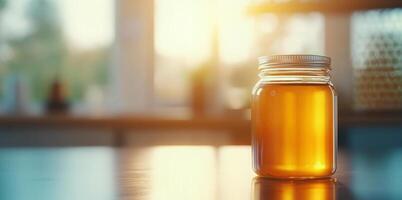 A jar filled with golden honey rests on a wooden table. Sunlight pours in through large windows, illuminating the organic honey. The warm atmosphere reflects a beekeeping environment. photo