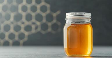 A clear jar of honey sits on a table with a sleek design, surrounded by a subtle honeycomb pattern in the background. This organic treat highlights the beauty of nature's sweetness. photo