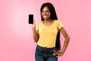 Great Application For Phone. Happy Black Female Showing Smartphone Empty Screen Posing On Blue Background In Studio, Smiling To Camera. New Mobile App Concept. Mockup photo