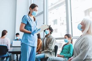 Diverse people sitting in line waiting for their turn to get shots at the hospital vaccination center. Nurse talking with patients in queue for antiviral flu vaccine photo