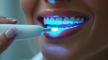 A person undergoing a teeth whitening procedure using a handheld device that emits blue light to enhance brightness at a dental clinic, showcasing a focus on dental care and aesthetics. photo