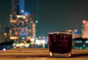 Glass of cola with urban night view bokeh in background photo