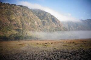 a dirt road in front of a mountain with fog photo