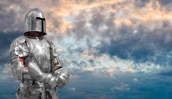 A knight stands with his hands on the hilt of his sword against a background of clouds. photo