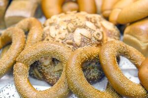 A variety of breads and rolls are displayed on a table. The breads are of different shapes and sizes, and some of them have sesame seeds on them. photo