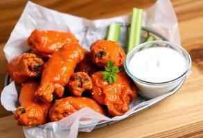 A basket of crispy, spicy Buffalo chicken wings, coated in a tangy, buttery hot sauce, served with a side of cool and creamy ranch dressing for dipping photo