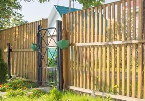 A wooden fence with a gate and a green plant photo