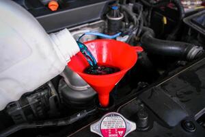 Pouring coolant liquid into a funnel of car radiator , Radiator coolant liquid changing in auto repair garage , Car maintenance concept photo