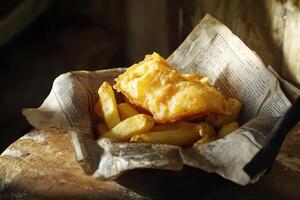 A traditional serving of English fish and chips presented in a folded piece of faux newspaper, styled for authenticity. photo