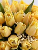 A stunning bouquet of vibrant yellow tulips fills the frame with their fresh blooms and soft petals, accented beautifully by a subtle string of pearls for an elegant touch photo