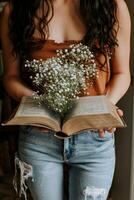 In a warm, inviting space, a stylish model gently holds an open book adorned with lush flowers, blending elegance with a passion for literature. The sunlight softly enhances the tranquil ambiance photo