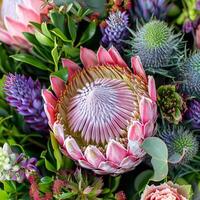 This close-up showcases a stunning collection of exotic flowers, featuring a prominent protea surrounded by lush greenery and captivating colors. Nature's artistry is on full display photo