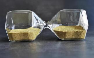 Laying sideway transparent Hourglass with golden Sand, sand glass in dark background, Time Stop or balance time concept, for advertising photo