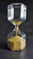 Close up transparent Hourglass with Falling golden Sand in dark background, Every second count, running out of time or passage of time concept photo