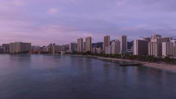 Serene aerial view of Waikiki Beach purple sunset in Honolulu with a slow pan, showing the skyline, Royal Hawaiian Hotel, calm ocean, and distant mountains. video
