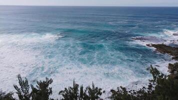 Aerial view of Oahu, Hawaii, showing turquoise waves crashing on rocky shores, lush coastal greenery, and a hazy horizon in the distance. video