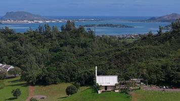 Aerial view of Byodo In Temple surrounded by lush greenery, with Kaneohe Bay, small islands, and distant hills visible in the background. video