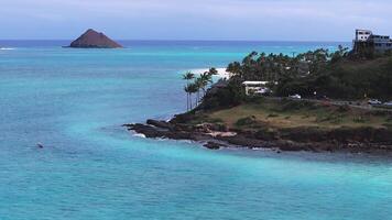 Aerial view of Lanikai Beach on Oahu Island, Hawaii, with turquoise waters, white sand, Mokulua Islands, lush greenery, and a paddleboarder gliding. video