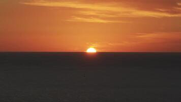 A tranquil sunset over the ocean with vibrant orange and red hues. A sailboat moves gently on calm waters, creating a peaceful and dynamic scene. video