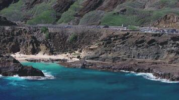Sweeping aerial view of a Halona Beach Cove rugged coastal cliff on Oahu, Hawaii, with ocean waves, greenery, and visitors at a lookout area with parked cars. video