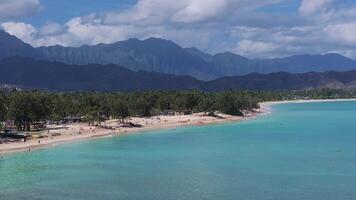 Aerial view of a Kailua beach on Oahu Island, Hawaii, with turquoise waters, paddleboarders, small boats, lush greenery, and rugged mountains in the background. video