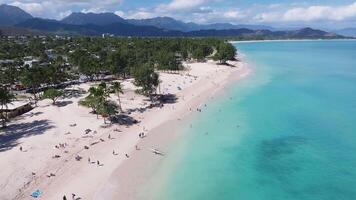 Aerial view of a Kailua beach on Oahu, Hawaii, featuring turquoise waters, beachgoers, a paddleboarder, lush greenery, and the Ko olau mountain range. video