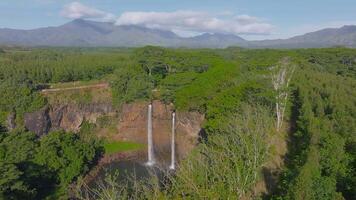 Aerial view of Wailua Falls on Kauai Island, Hawaii, with twin waterfalls flowing into a pool, surrounded by tropical vegetation and mountains. video