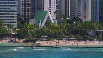 Aerial view of Waikiki Beach in Honolulu, Hawaii, with turquoise waters, beachgoers, colorful umbrellas, and a backdrop of high rise buildings. video