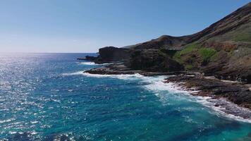 Aerial view of Oahu Island's coastline, featuring a rocky mountain ridge, ocean waves crashing on the shore, and a road with moving vehicles. video