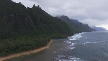Aerial view of Napali Coast on Kauai Island, Hawaii, with green cliffs, sandy beaches, rolling waves, and an overcast sky creating a moody scene. video
