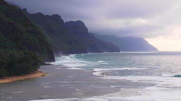 Serene aerial view of Napali Coast on Kauai Island, Hawaii, with misty cliffs, rolling ocean waves, sandy shoreline, and an overcast sky. video