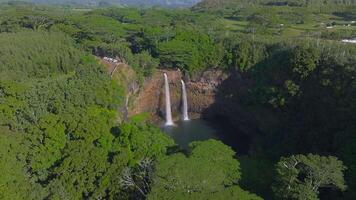 Twin waterfalls flow from a rocky cliff into a serene pool, surrounded by lush greenery on Kauai Island, Hawaii, with visible water motion and mist. video