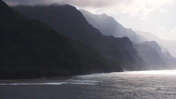 A slow, sweeping aerial pan of the Napali Coast on Kauai Island, Hawaii, showcasing jagged cliffs, lush green mountains, and shimmering ocean waters. video