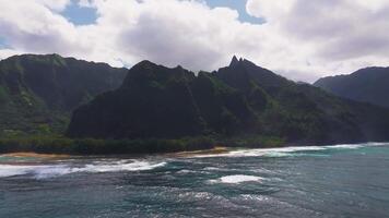 Aerial view of Napali Coast on Kauai Island, Hawaii, with jagged green cliffs, turquoise waters with whitecaps, and a narrow golden beach below. video