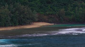 A serene aerial view of a secluded beach on Kauai Island, Hawaii, with lush greenery, calm turquoise waters, and gentle waves rolling onto the shore. video