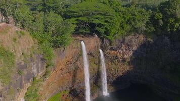 Aerial view of Wailua Falls on Kauai Island, Hawaii. Twin waterfalls flow over a rocky cliff into a pool, surrounded by lush greenery and a viewing area. video