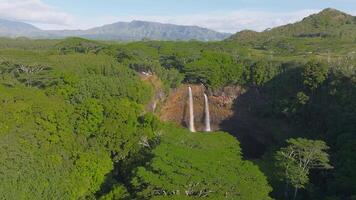 Aerial view of Wailua Falls on Kauai island, Hawaii, with twin waterfalls flowing into a pool, surrounded by forests and distant mountains. video
