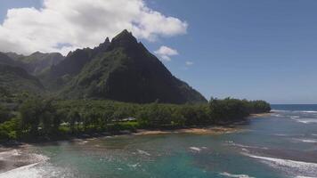 Aerial view of Napali Coast on Kauai Island, Hawaii, with jagged cliffs, lush greenery, a pristine beach, and turquoise waves rolling to shore. video
