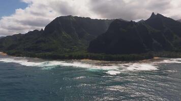 Aerial view of Napali Coast on Kauai Island, Hawaii, showing jagged cliffs, turquoise ocean, sandy beaches, and lush greenery under a cloudy sky. video