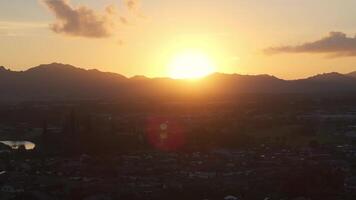 Aerial view of Kauai island during sunset, showing jagged mountains, a small town, and lush greenery with warm golden light and slow motion pan. video